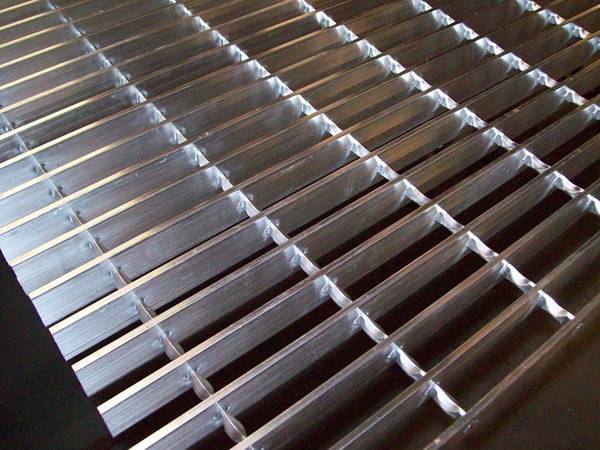 A piece of aluminum swage locked grating on black ground.