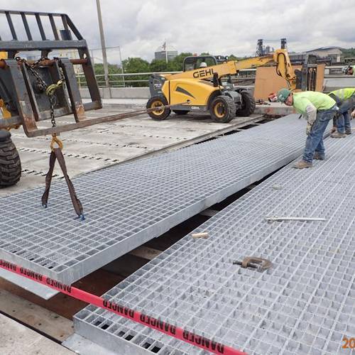 Several workers are paving steel grating on bridge decking.