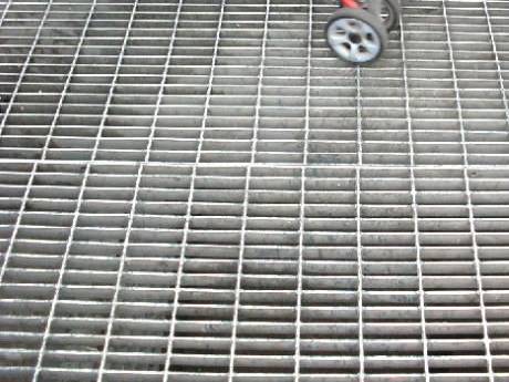 A man pushing a baby carriage through the floor made of dense steel grating.