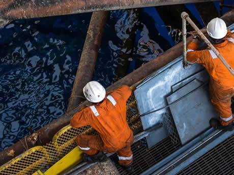 Standing on the steel grating drilling platform, two workers leaning on the guardrail to see the sea.