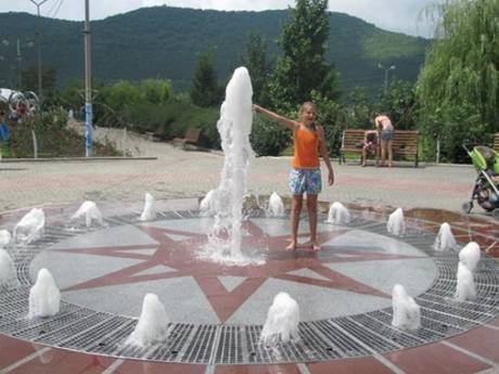 A girl is playing on the square with fountain.