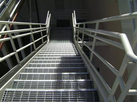 A stair made of straight stair tread steel grating is used in a factory.