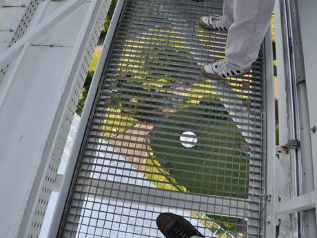 A people is standing on the steel grating walkway of roof.